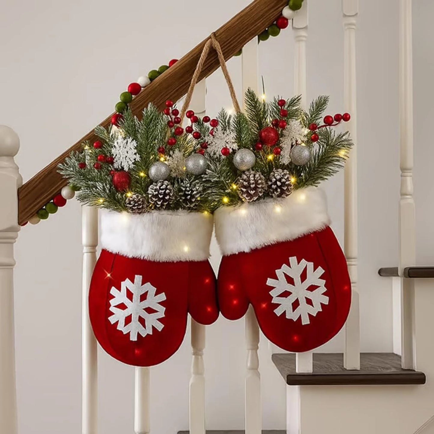 Glove-shaped red mitten garland with white fur cuff, pine boughs, berries, pinecones and lights on a staircase railing.