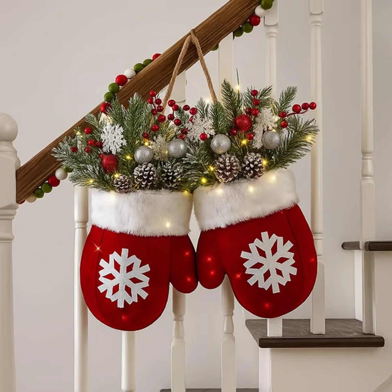 Glove-shaped red mitten garland with white fur cuff, pine boughs, berries, pinecones and lights on a staircase railing.