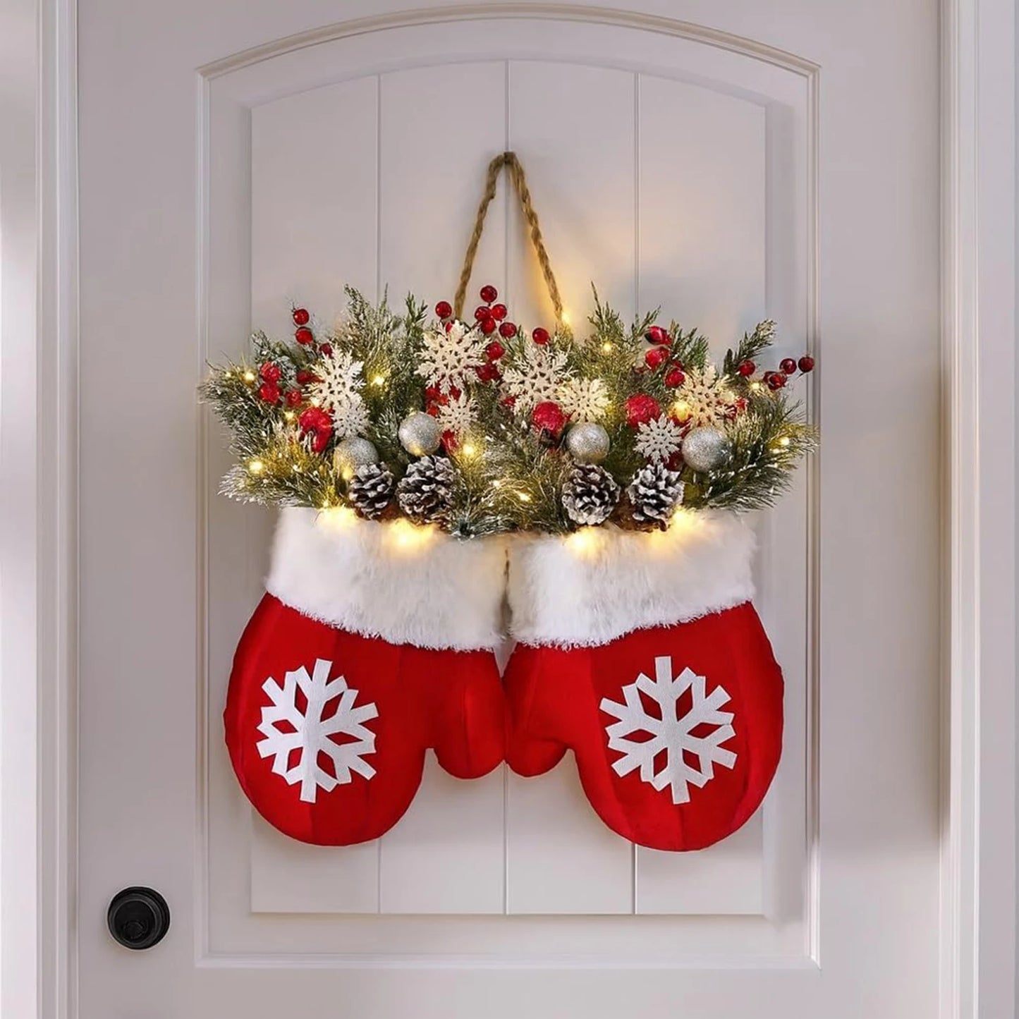 Glove-shaped red mitten garland on a door, featuring a snowy pine wreath with berries, pinecones and warm lights.