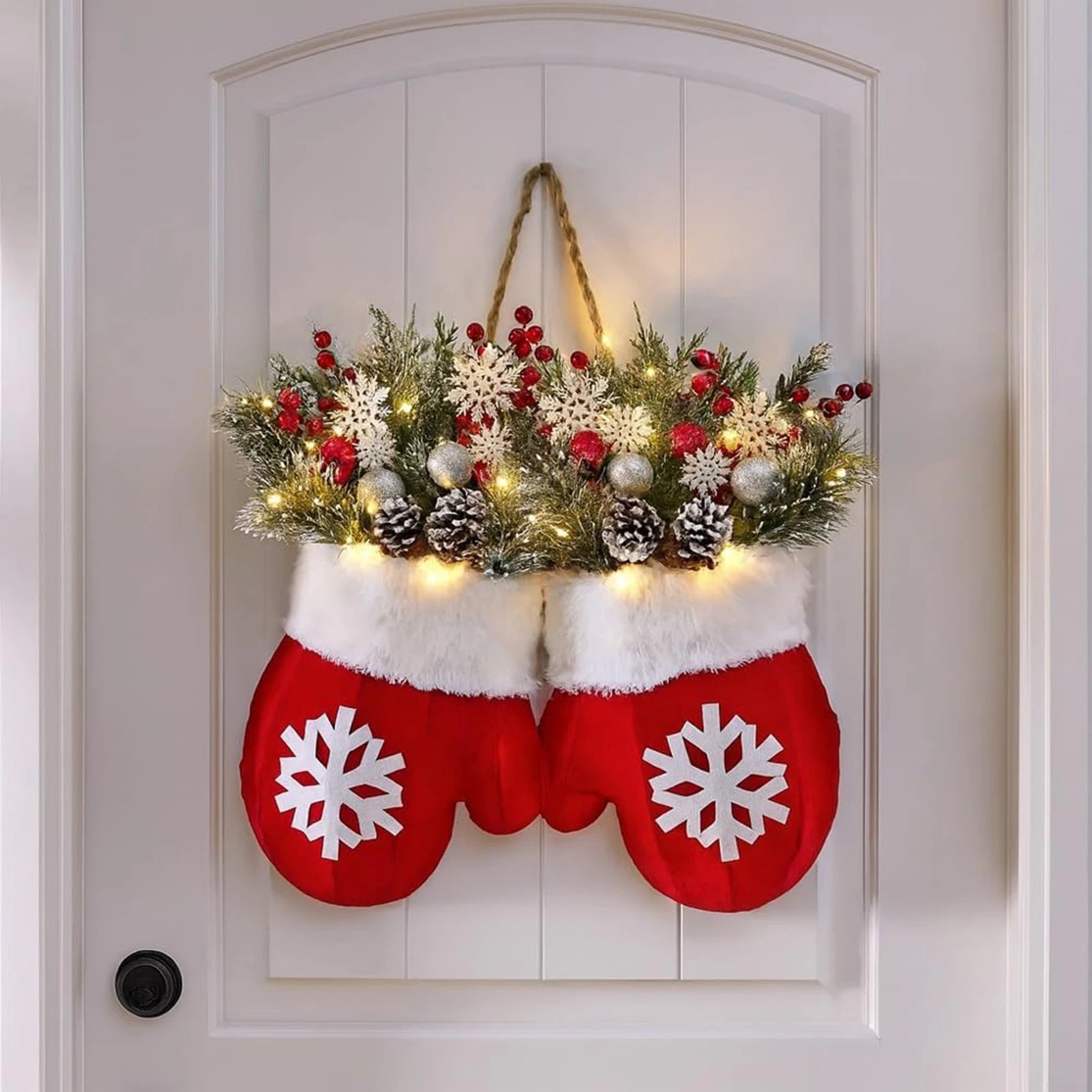 Glove-shaped red mitten garland on a door, featuring a snowy pine wreath with berries, pinecones and warm lights.